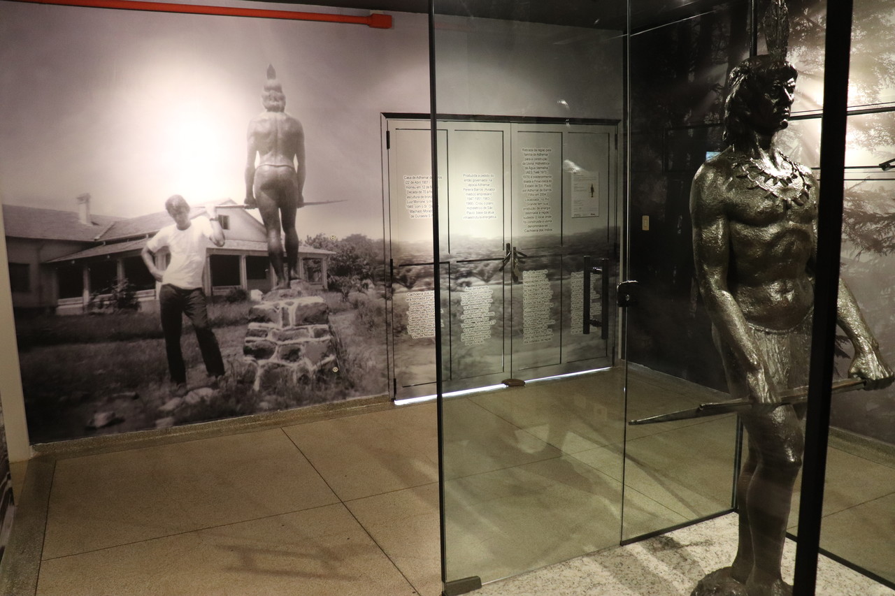 Foto perfilada da estátua de bronze do indío, ao fundo uma foto antiga da estatua no local original com uma pessoa do lado